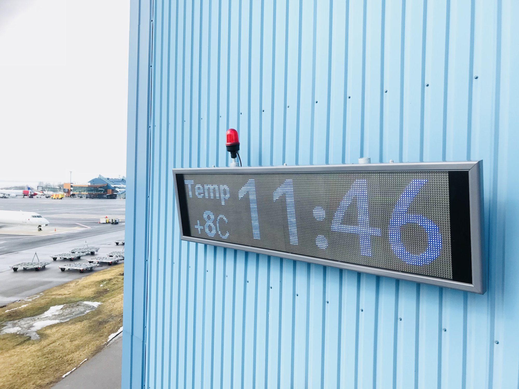 Wall-mounted Ampron LED display on a hangar at Tallinn Airport showing time and temperature.