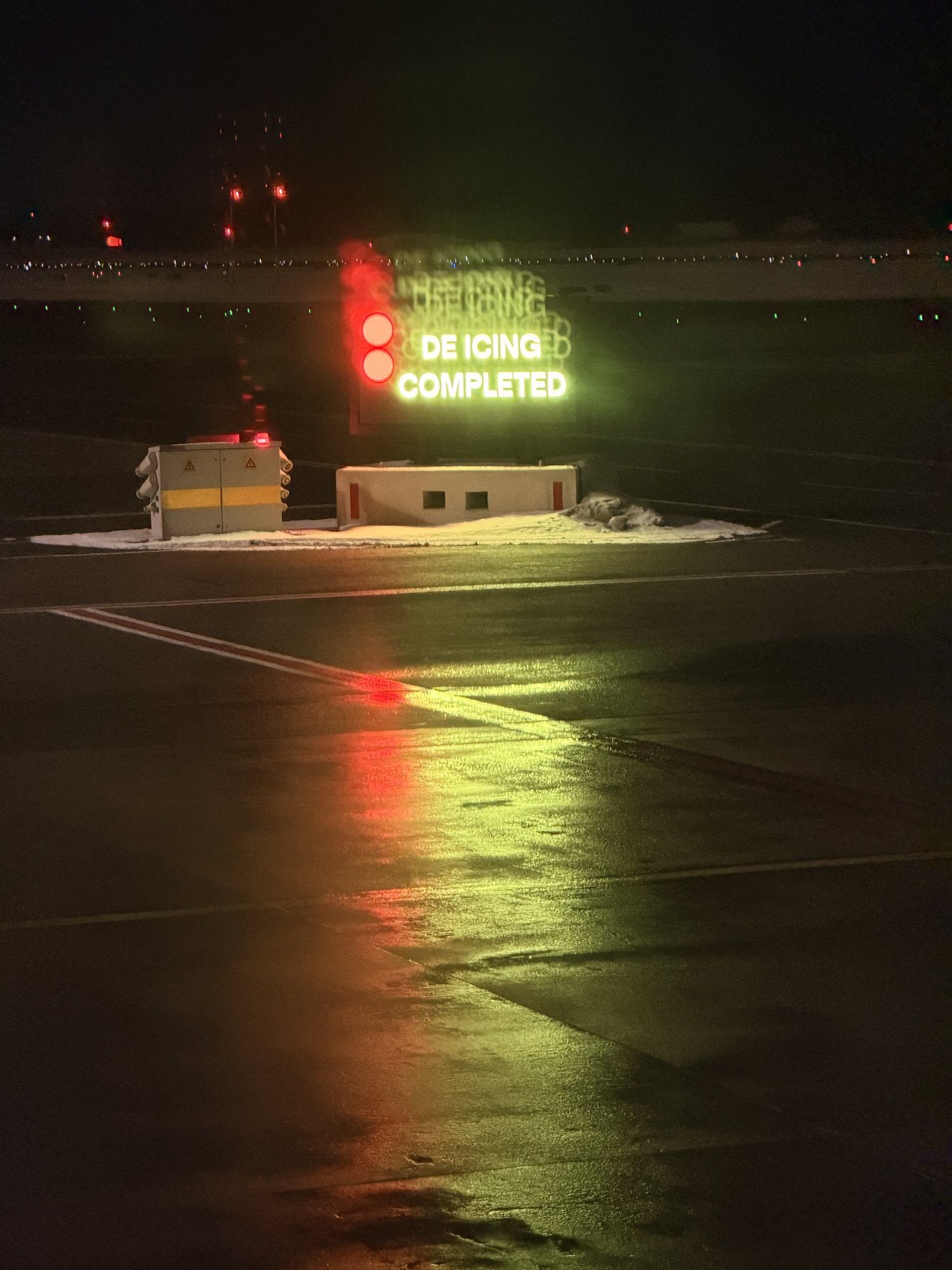 De-icing pad display at night showing DE ICING COMPLETED, its light reflected on the wet apron.