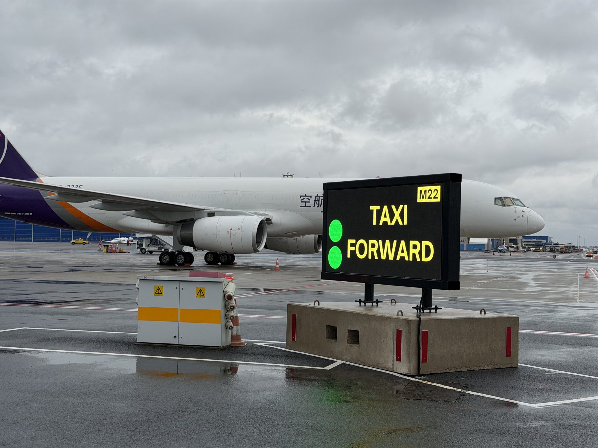 Stationary Ampron LED display on a concrete base at the Tallinn Airport de-icing pad showing TAXI FORWARD with two green lights, a cargo aircraft behind.